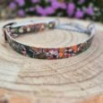 Printed BioThane martingale dog collar with vibrant graphic design, displayed on wooden surface with purple flowers behind.