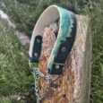 Handmade BioThane dog collar with printed half check design in turquoise and black, attached to wooden post with chain lead.