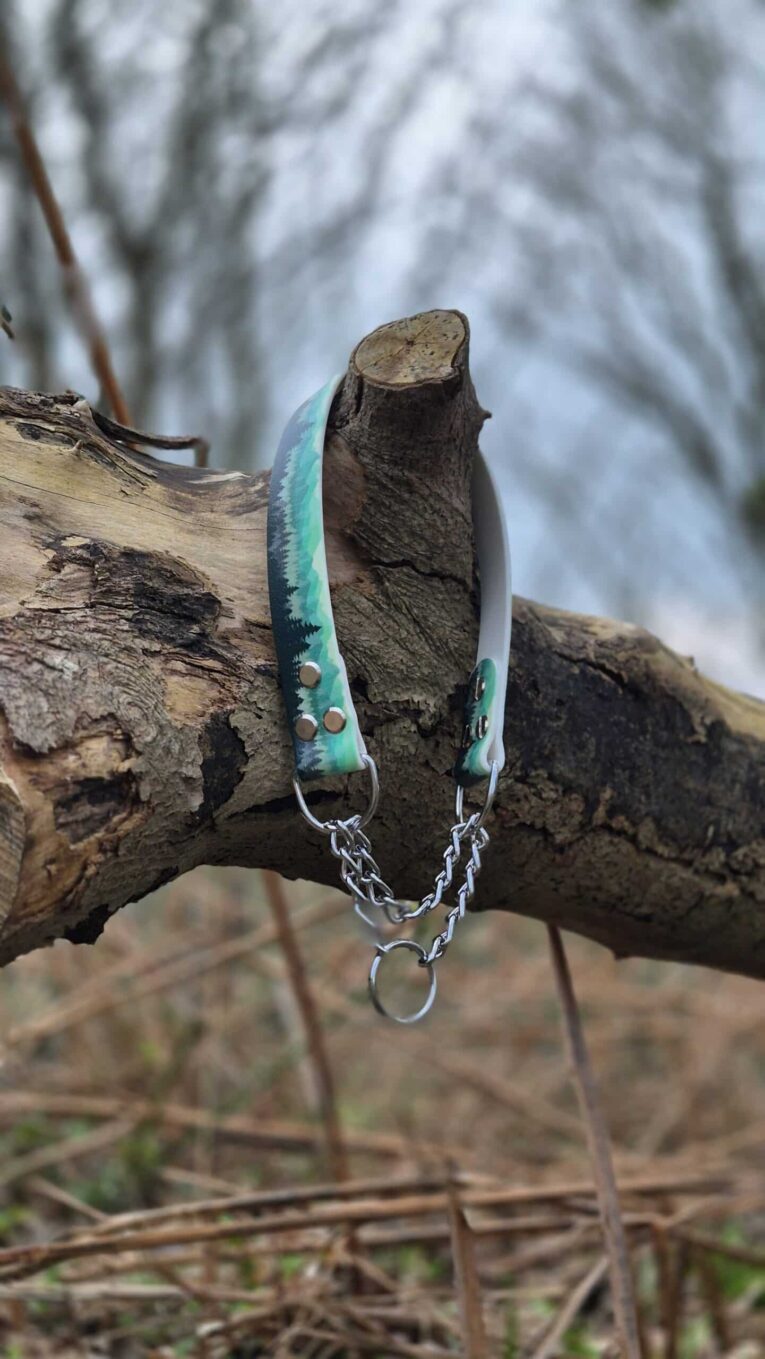 Handmade BioThane dog collars in turquoise and dark tones with metal hardware, displayed on a wooden branch.
