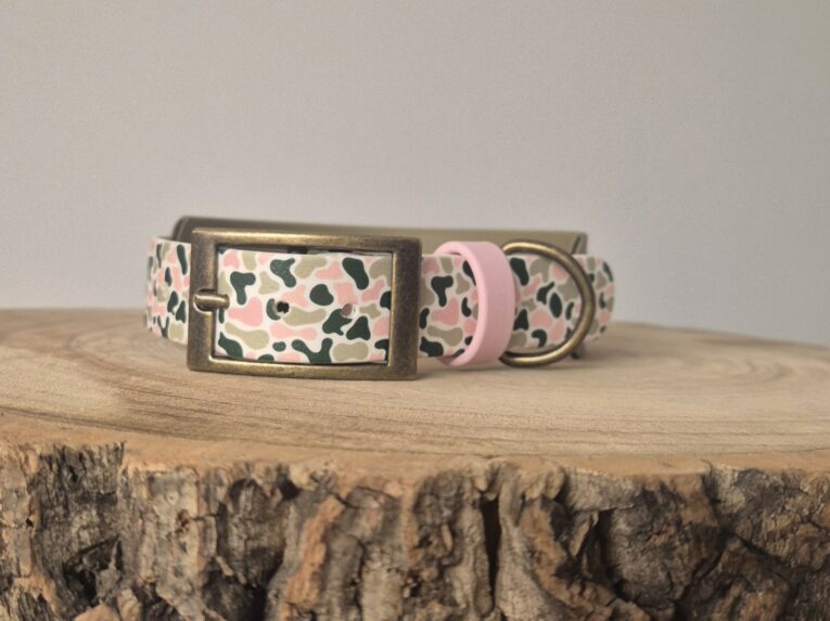 Printed hound collar in pink, cream and black patterned BioThane with bronze hardware, displayed on wooden surface.