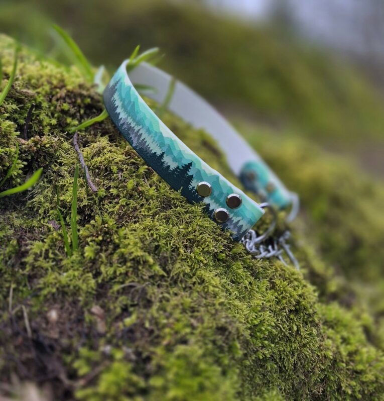 Printed martingale dog collar in turquoise with forest design and metal fixtures, displayed on moss.