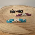 Three biothane quick release buckles in black, burgundy, and turquoise with metal hardware, displayed on wood.