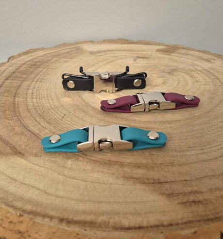 Three biothane quick release buckles in black, burgundy, and turquoise with metal hardware, displayed on wood.