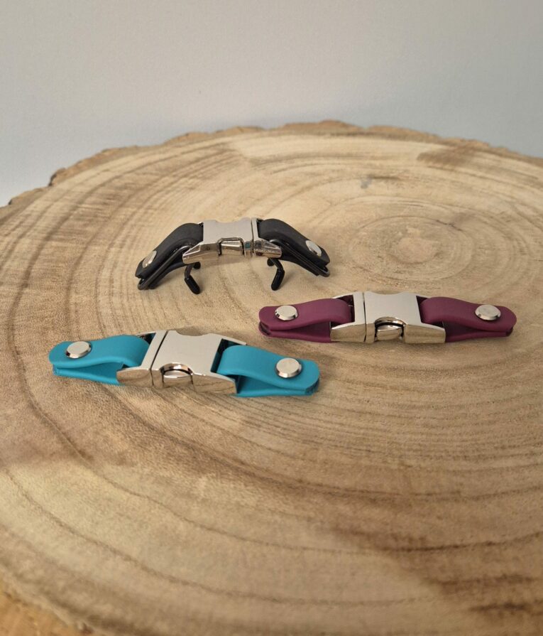 Three biothane quick release buckles in black, turquoise, and burgundy BioThane, displayed on wood.