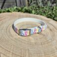 Colourful rainbow leopard print handmade BioThane dog collar with chrome buckle on wooden surface.