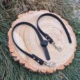 Black BioThane dog lead with textured grip handles and metal fittings, displayed on wood slice.