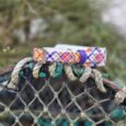 Vibrant tartan-patterned handmade dog collar displayed on weathered rope, showcasing colourful woven design with metal hardware.