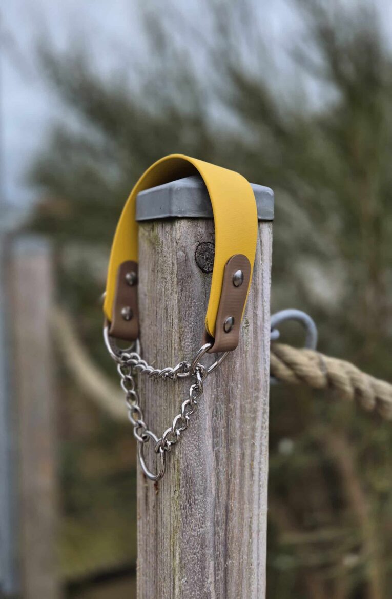 Waterproof martingale dog collar with yellow BioThane handle and brown BioThane tabs, secured to wooden post with chain.