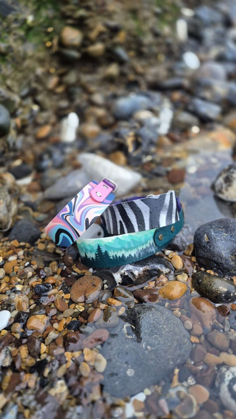 Colourful handmade BioThane dog collars displayed on pebbles, showcasing vibrant patterns and waterproof design.