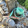 Turquoise waterproof printed BioThane dog lead coiled beside a wooden post on pebbled ground.