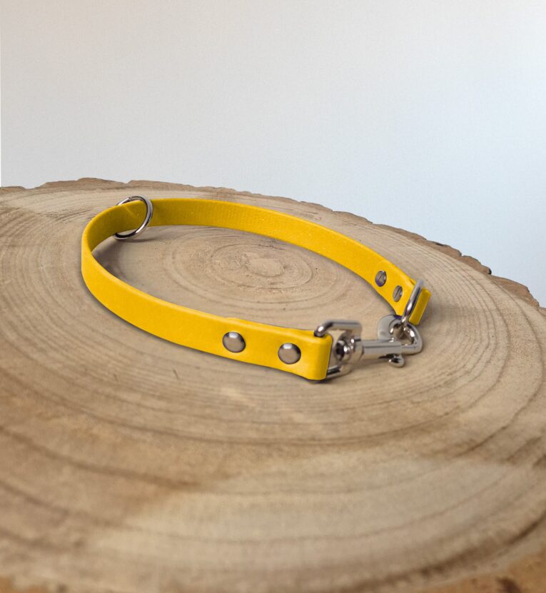 Bright yellow waterproof slip collar with metal fittings and D-ring, displayed on natural wood