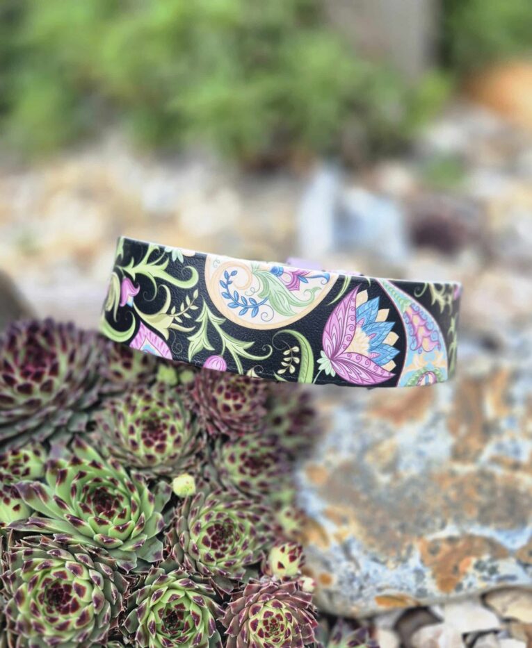 Vibrant handmade BioThane dog collar with intricate floral and botanical patterns in pink, blue, green and black against natural garden stones.