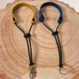 Two handmade BioThane wrist straps, lanyards with yellow and navy headbands, black cords, and metal hardware on natural wood.