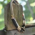 Handmade paracord dog collar with striped handle wrap, looped over weathered wooden post in garden setting.