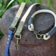 Three handmade BioThane dog lead in blue, cream and striped designs with brass fittings, displayed on a dark stone surface.