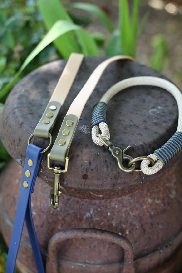 Three handmade BioThane dog lead in blue, cream and striped designs with brass fittings, displayed on a dark stone surface.