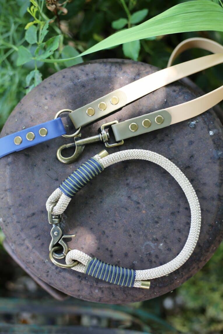 Handmade BioThane dog leads in beige, nave and olive with antique brass fittings, displayed on slate.
