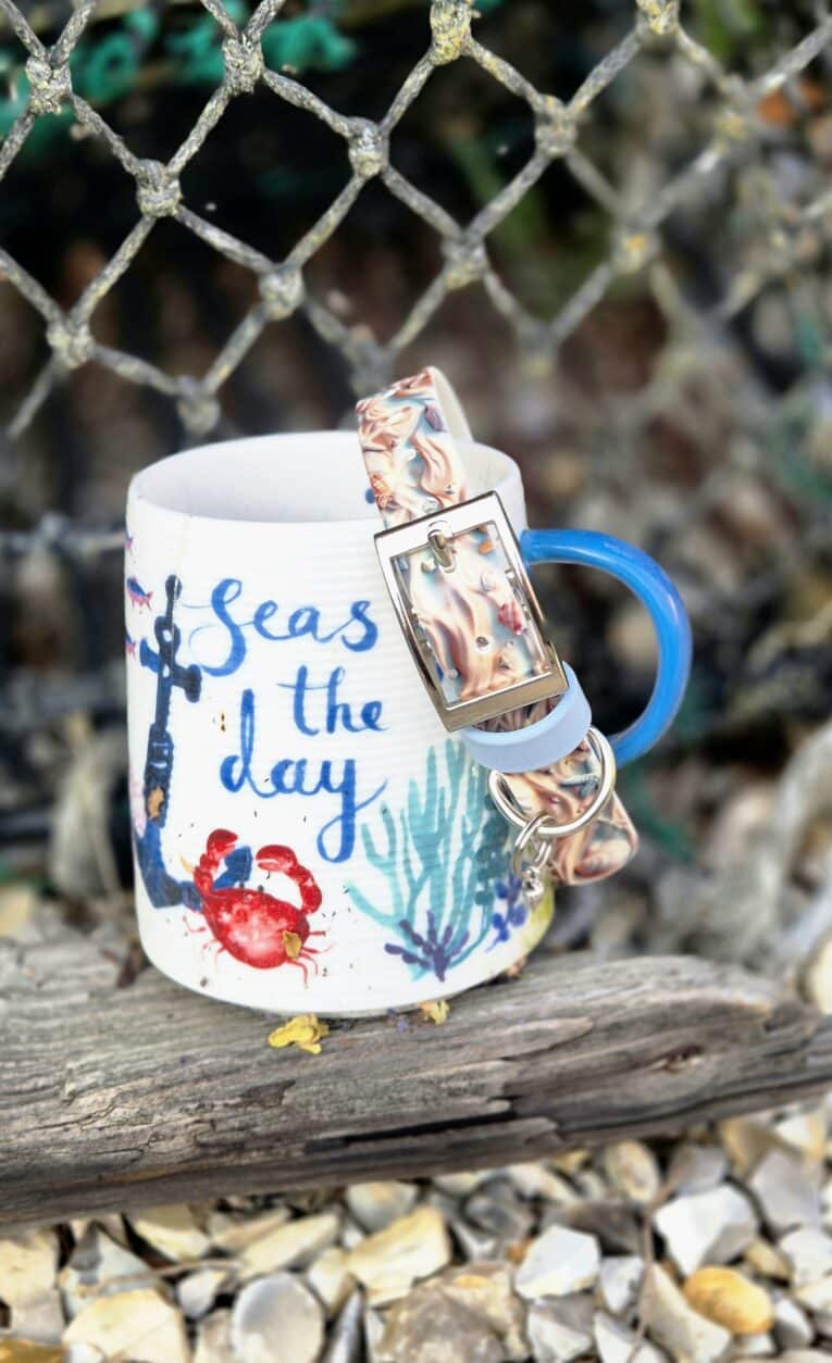 White mug with nautical design and blue handle, featuring a charm bracelet with sea-themed charms attached.