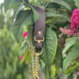 Brown BioThane martingale collar with solid brass chain and hardware, displayed amongst flowering shrubs.