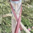 Burgundy BioThane dog collar with leather-look handle, displayed on wooden garden post surrounded by foliage.