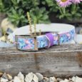 Handmade BioThane dog collar with butterfly print design, featuring purple hardware and silver buckle, displayed on weathered wood.