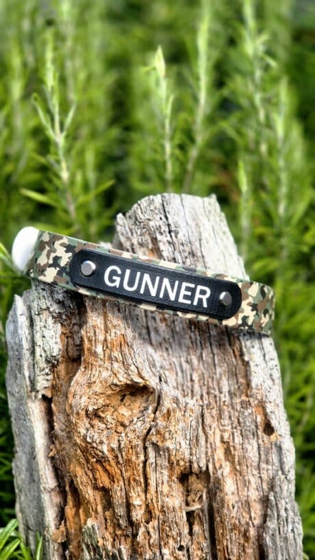 Gundog collar with camouflage BioThane and black nameplate reading 'GUNNER' on weathered wood post