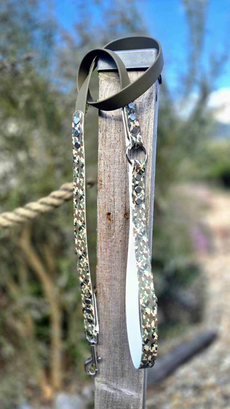 Handmade BioThane dog collar with patterned webbing and metal hardware, displayed on weathered wood post outdoors.