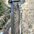 Handmade BioThane dog collars in camouflage pattern with blue buckle and metal D-ring displayed on wooden post.