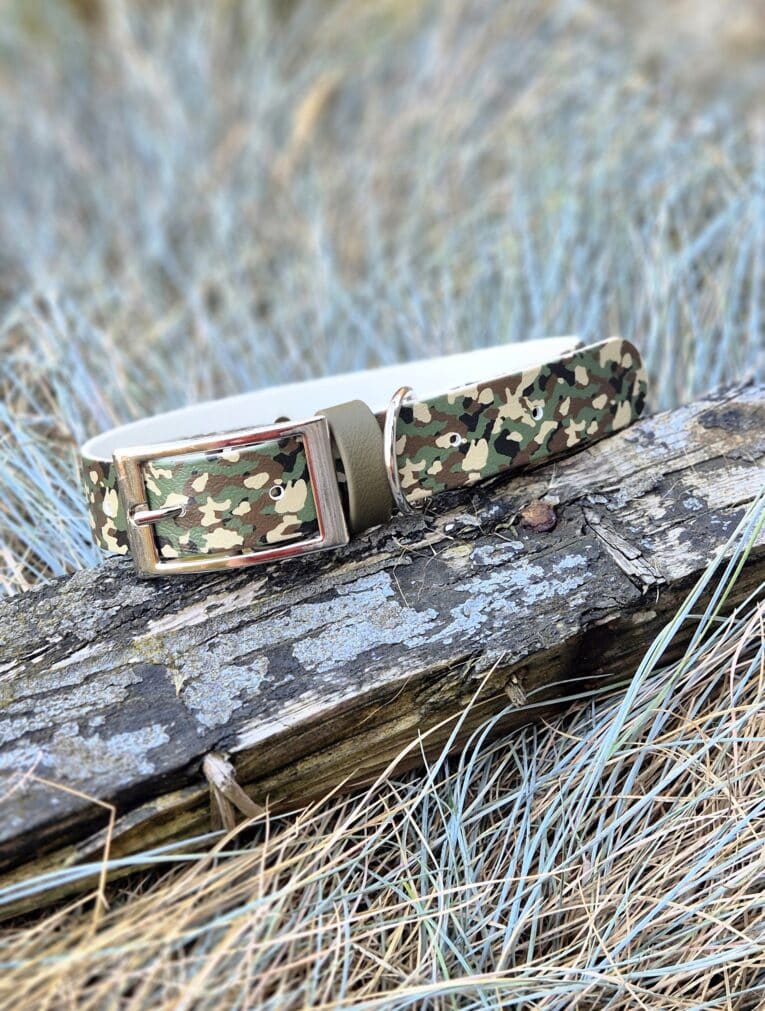 Handmade BioThane dog collar in camouflage pattern with metal buckle, displayed on weathered log.