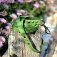 Bright lime-green handmade BioThane dog collar with metal hardware, draped on weathered wood post beside purple flowers.