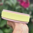 Hand holding pastel pink and yellow handmade BioThane dog collars against a blurred garden backdrop.
