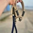 Hand holding a handmade paracord dog collar and biothane lead set in tan and navy, displayed on a beach.