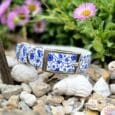 Handmade BioThane dog collar with blue and white nautical print design, displayed on pebbles with flowers.