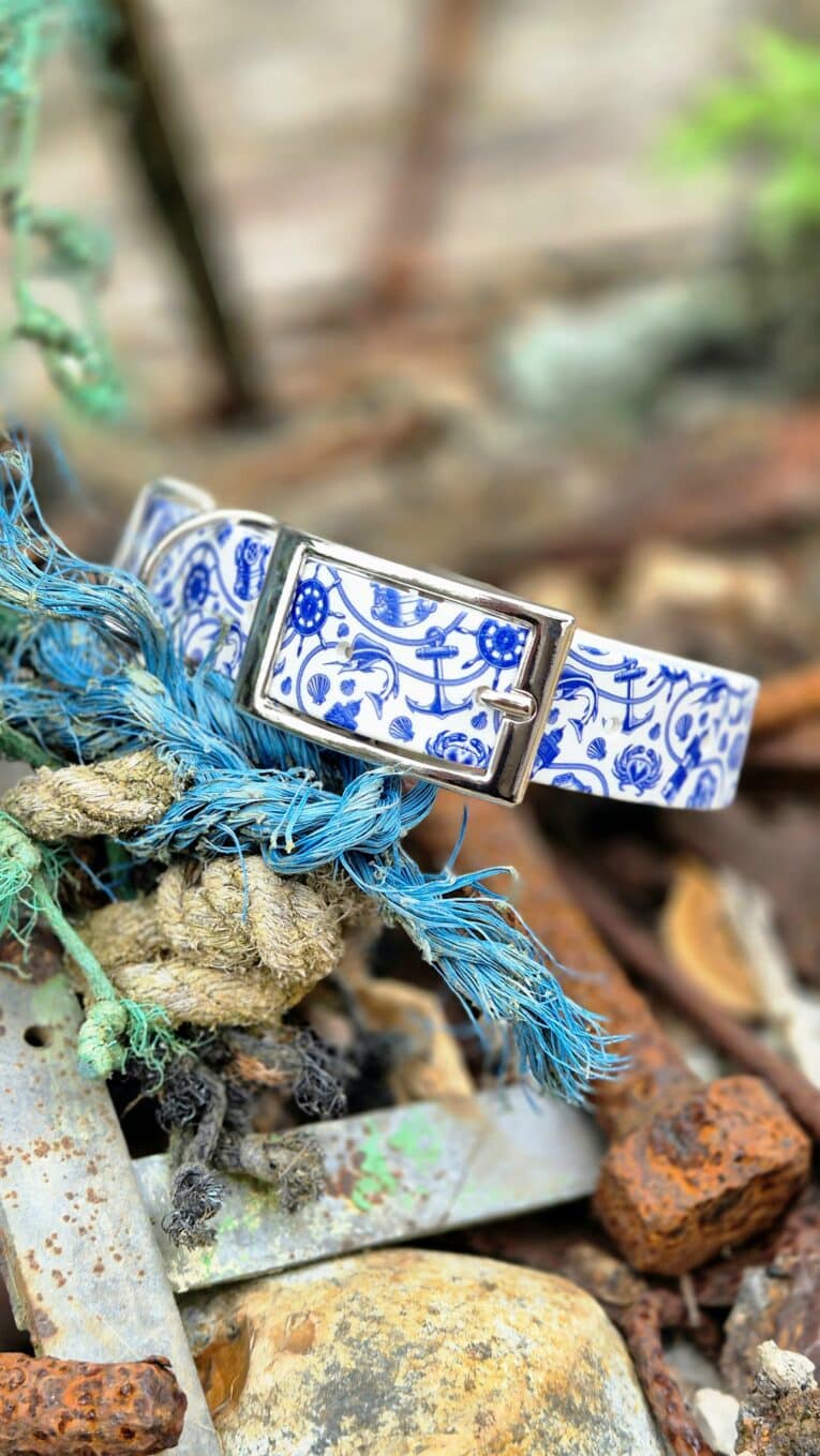 Nautical-themed handmade BioThane dog collar with blue and white maritime print, silver buckle, displayed on rope and stones.