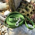 Bright green waterproof BioThane dog lead coiled on a stone, displaying metal hardware and textured surface detail outdoors.