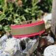 Pink and khaki handmade BioThane hound collar displayed on weathered stone in a garden setting.