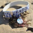 Tails of the Coast BioThane collar and matching tag on sand, featuring blue and white nautical patterns.