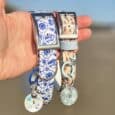 Two Tails of the coast BioThane dog collars with matching ID tags held in hand against a beach backdrop.