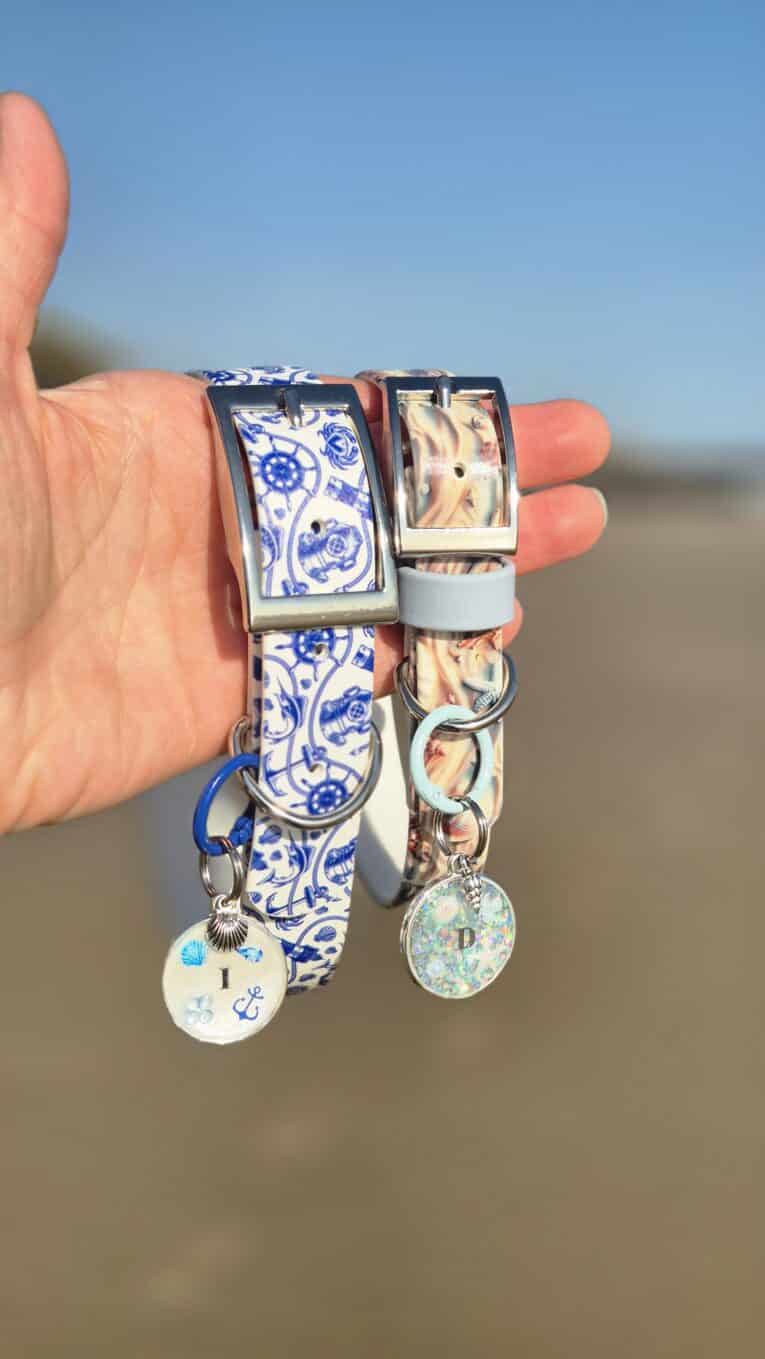 Two Tails of the coast BioThane dog collars with matching ID tags held in hand against a beach backdrop.