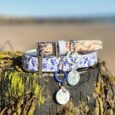 Two handmade BioThane dog collars with blue and white porcelain patterns and matching tag charms displayed on a coastal rock.