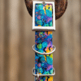 Vibrant handmade BioThane dog collar with tropical floral print, silver hardware, and matching tag holder displayed on rustic metal hook.