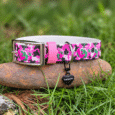 Bright pink pumpkin-print handmade BioThane dog collar with metal buckle and heart charm, displayed on stone and grass.